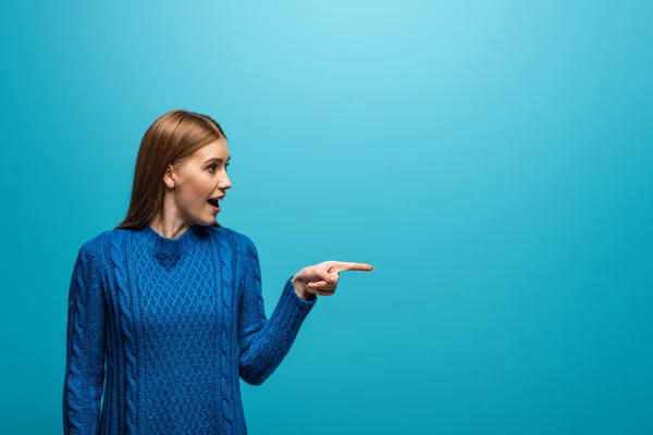 Bella donna eccitata in maglia blu maglione che punta a qualcosa, isolato su blu — Foto stock