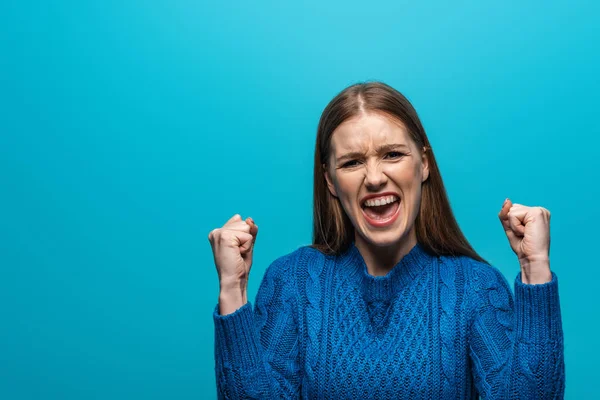 Successful woman in blue knitted sweater celebrating triumph, isolated on blue — Stock Photo