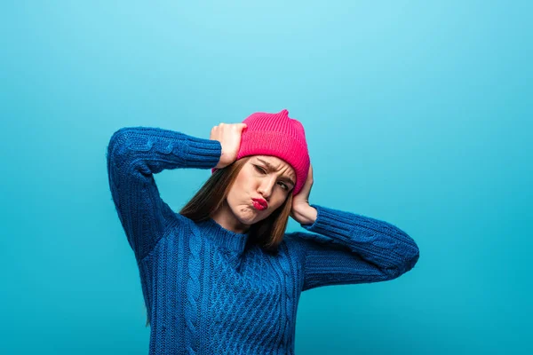 Atraente mulher cética em camisola de malha e chapéu rosa, isolado em azul — Fotografia de Stock