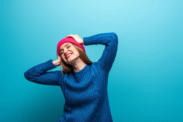 Jolie femme heureuse en pull tricoté et chapeau rose, isolé sur bleu — Photo de stock