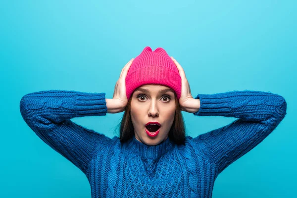 Attractive shocked woman in knitted sweater and pink hat, isolated on blue — Stock Photo