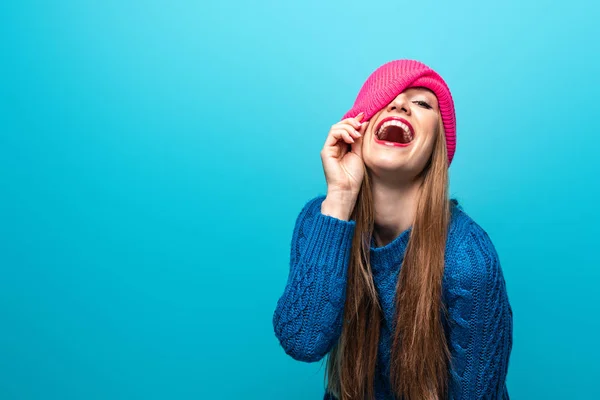 Atraente mulher engraçada rindo em camisola de malha e chapéu rosa, isolado em azul — Fotografia de Stock