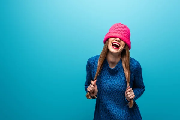 Divertida mujer riendo en suéter de punto con sombrero rosa en los ojos, aislado en azul - foto de stock