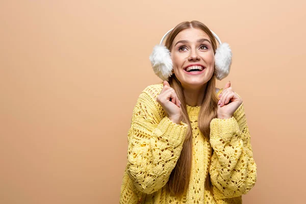 Beautiful excited woman in yellow sweater and ear warmers, isolated on beige — Stock Photo