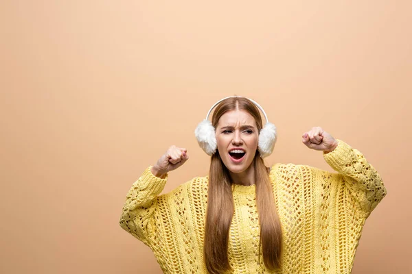 Beautiful cheerful woman dancing in yellow sweater and earmuffs, isolated on beige — Stock Photo