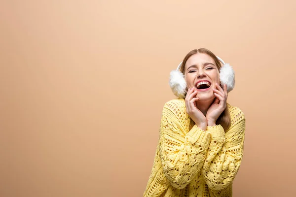 Красива жінка сміється в жовтому светрі і вухах, ізольована на бежевому — стокове фото
