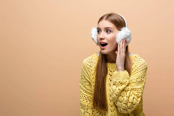 Attractive excited woman in yellow sweater and earmuffs, isolated on beige — Stock Photo