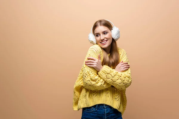 Mujer sonriente fría en suéter amarillo y calentadores de oídos, aislada en beige - foto de stock