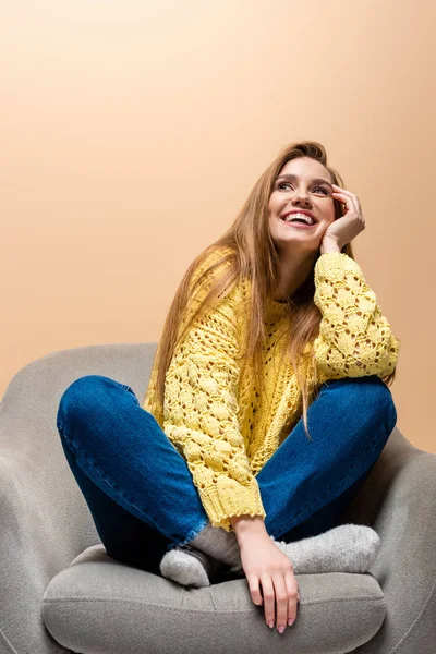 Schönes lachendes Mädchen in gelbem Pullover auf Sessel sitzend, isoliert auf beige — Stockfoto