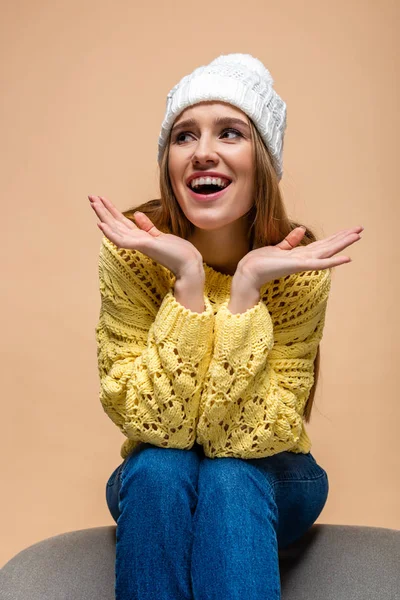 Beautiful positive woman in yellow sweater and hat sitting on armchair, isolated on beige — Stock Photo