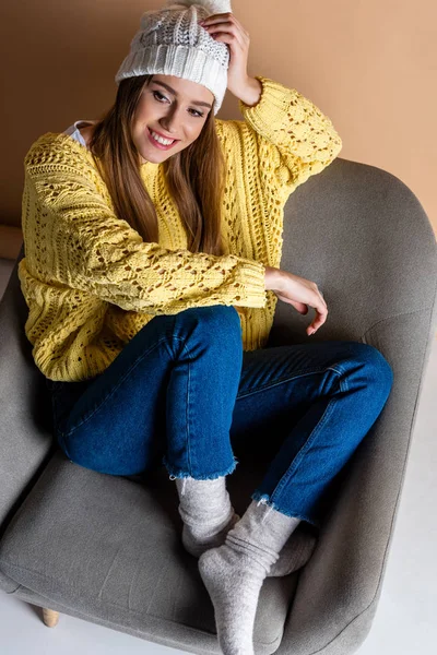 Mulher alegre em suéter amarelo e chapéu sentado em poltrona no bege — Fotografia de Stock