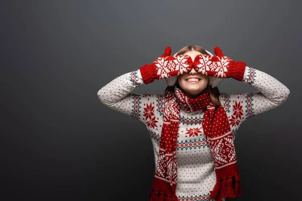 Mujer feliz en jersey de Navidad, bufanda, manoplas y orejeras cerrando los ojos, aislado en gris - foto de stock