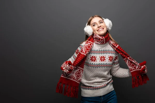 Attraktive lächelnde Frau in Weihnachtspullover, Schal, Handschuhe und Ohrenschützer, isoliert auf grau — Stockfoto