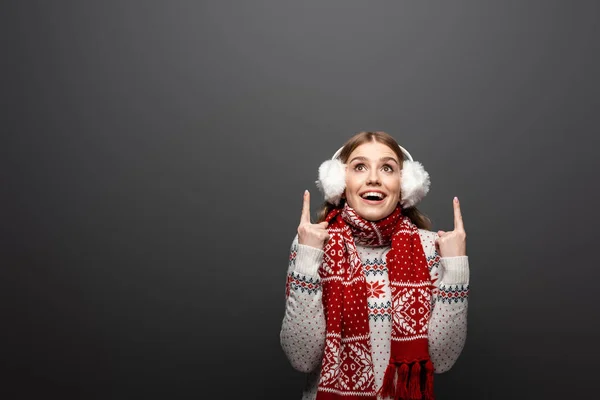 Mulher sorridente atraente em camisola de Natal, cachecol e auriculares apontando para cima, isolado em cinza — Fotografia de Stock