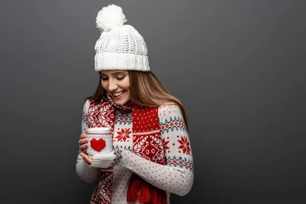 Улыбающаяся девушка в шляпе и свитере с чашкой кофе, изолированная на сером — стоковое фото