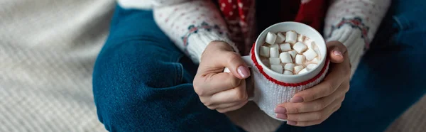 Cropped view of woman holding cup of cocoa with marshmallow and sitting on blanket — Stock Photo