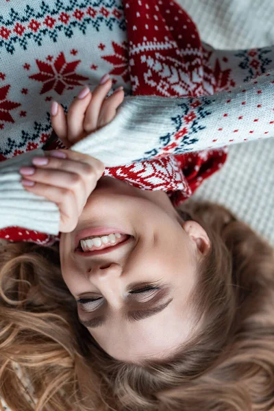 Веселая женщина с закрытыми глазами в теплом свитере и шарфе, лежащих на одеяле — стоковое фото