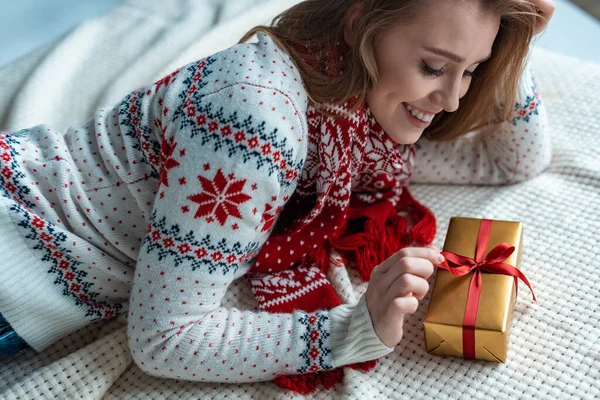 Happy woman in warm sweater holding gift box and lying on blanket — Stock Photo