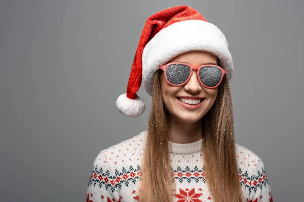 Bella donna felice in maglione di Natale, cappello di Babbo Natale e occhiali da sole, isolato su grigio — Foto stock