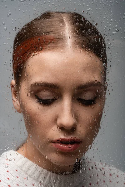 Triste mujer solitaria en gris, más allá de vidrio húmedo con gotas - foto de stock