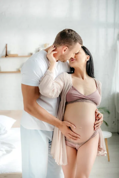 Handsome husband hugging and kissing his pregnant wife in bedroom — Stock Photo