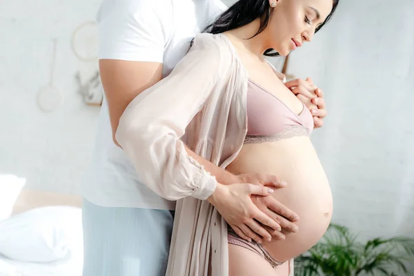 Муж обнимает свою прекрасную беременную жену в спальне — стоковое фото