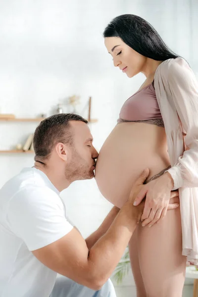 Marido feliz beijando barriga de sua esposa grávida no quarto — Fotografia de Stock