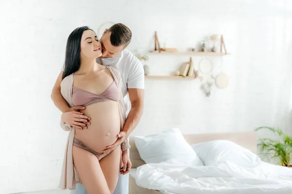 Щасливий чоловік обіймає і цілує свою красиву вагітну дружину в ліжку — стокове фото