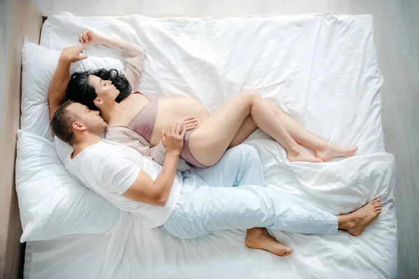 Вид зверху чоловіка обіймає свою вагітну дружину під час сну на ліжку — стокове фото
