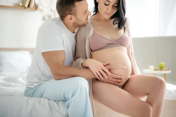 Schöner Mann umarmt Bauch seiner schwangeren Frau im Bett — Stockfoto