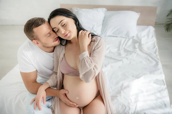 Mari souriant étreignant et embrassant sa femme enceinte au lit — Photo de stock