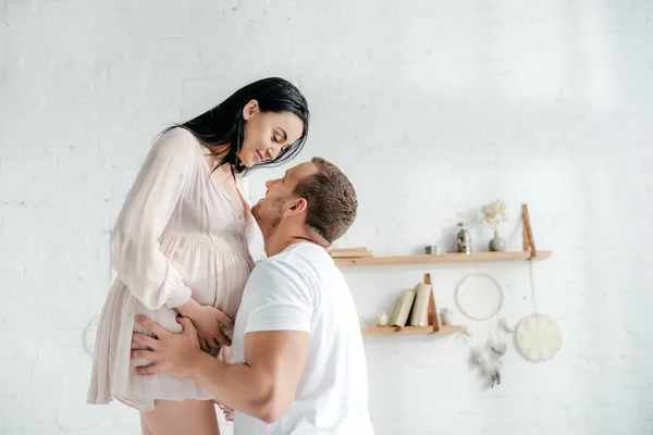 Marido guapo abrazando a su esposa embarazada en el dormitorio - foto de stock