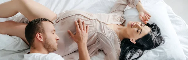 Tiro panorâmico de marido feliz abraçando sua atraente esposa grávida na cama — Fotografia de Stock