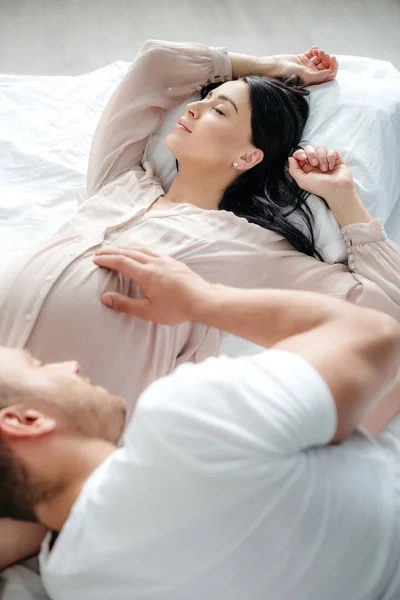 Счастливый муж обнимает свою прекрасную беременную жену в постели — стоковое фото