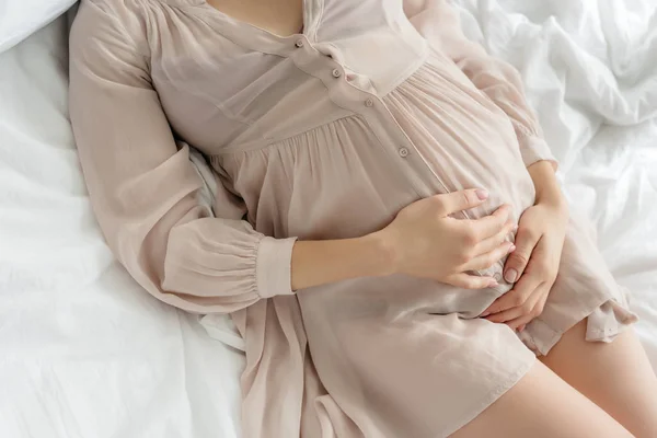 Обрізаний вид вагітної жінки в сусідньому дотику до живота, лежачи в ліжку — стокове фото