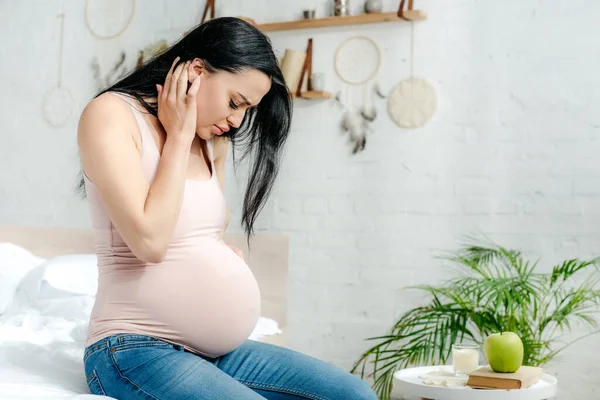 Worried pregnant woman having pain and looking at belly in bedroom — Stock Photo