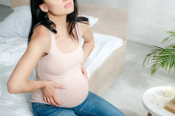 Vista recortada de la mujer embarazada preocupada teniendo dolor y tocando el vientre en el dormitorio - foto de stock