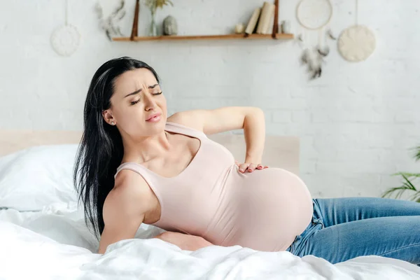 Worried pregnant woman having pain and touching tummy on bed — Stock Photo