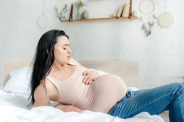 Worried pregnant girl having pain and touching belly in bedroom — Stock Photo