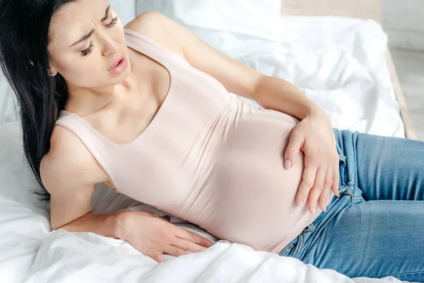 Беспокойная беременная женщина испытывает боль и трогает живот в спальне — стоковое фото