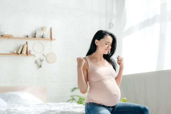 Emotional pregnant woman holding fists while sitting in bedroom — Stock Photo