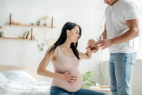 Man giving pill to pregnant woman having pain in bedroom — Stock Photo