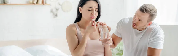 Frau mit Schmerztablette mit Wasser im Schlafzimmer mit Mann in der Nähe — Stockfoto