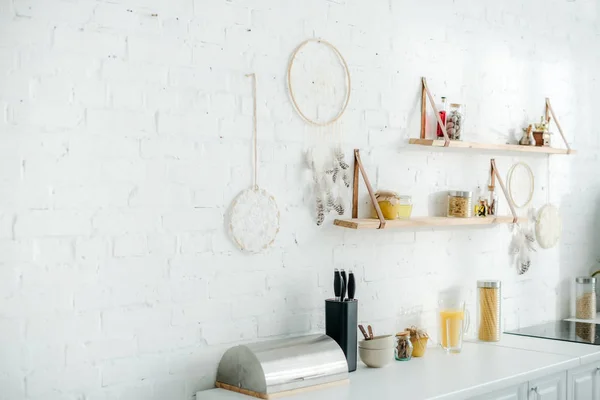 Attrapeurs de rêves et étagères en bois avec bocaux sur mur de briques blanches dans la cuisine — Photo de stock