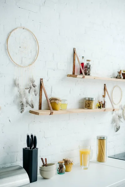 Dream catchers and wooden shelves with jars on white brick wall in kitchen — Stock Photo