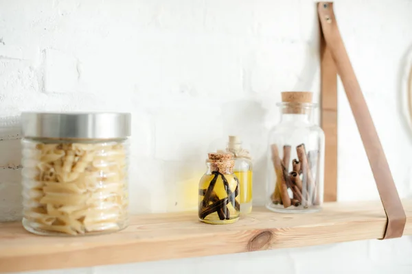 Étagères en bois avec épices et pâtes dans des bocaux sur mur de briques blanches dans la cuisine — Photo de stock