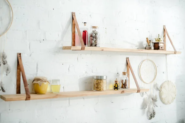 Dream catchers and wooden shelves with jars on white brick wall in kitchen — Stock Photo