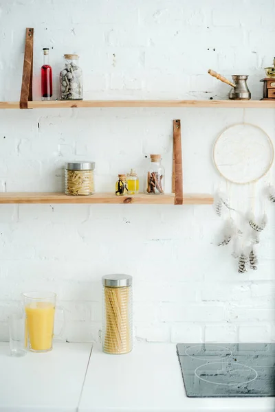 Stufa elettrica, raccoglitore di sogni e ripiani in legno con vasetti su parete in mattoni bianchi in cucina — Foto stock