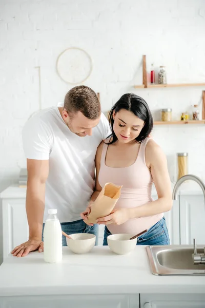 Feliz casal grávida com cereais e leite na cozinha — Fotografia de Stock