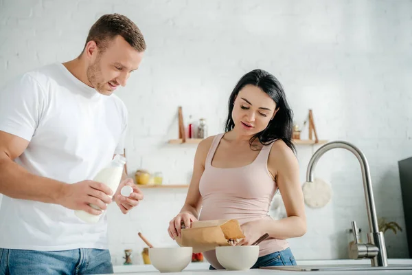 Happy pregnant couple making cereals with milk in kitchen — Stock Photo
